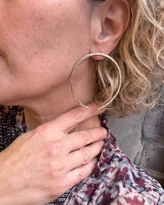 Close-up of a person wearing a gold hoop earring with a blurred background