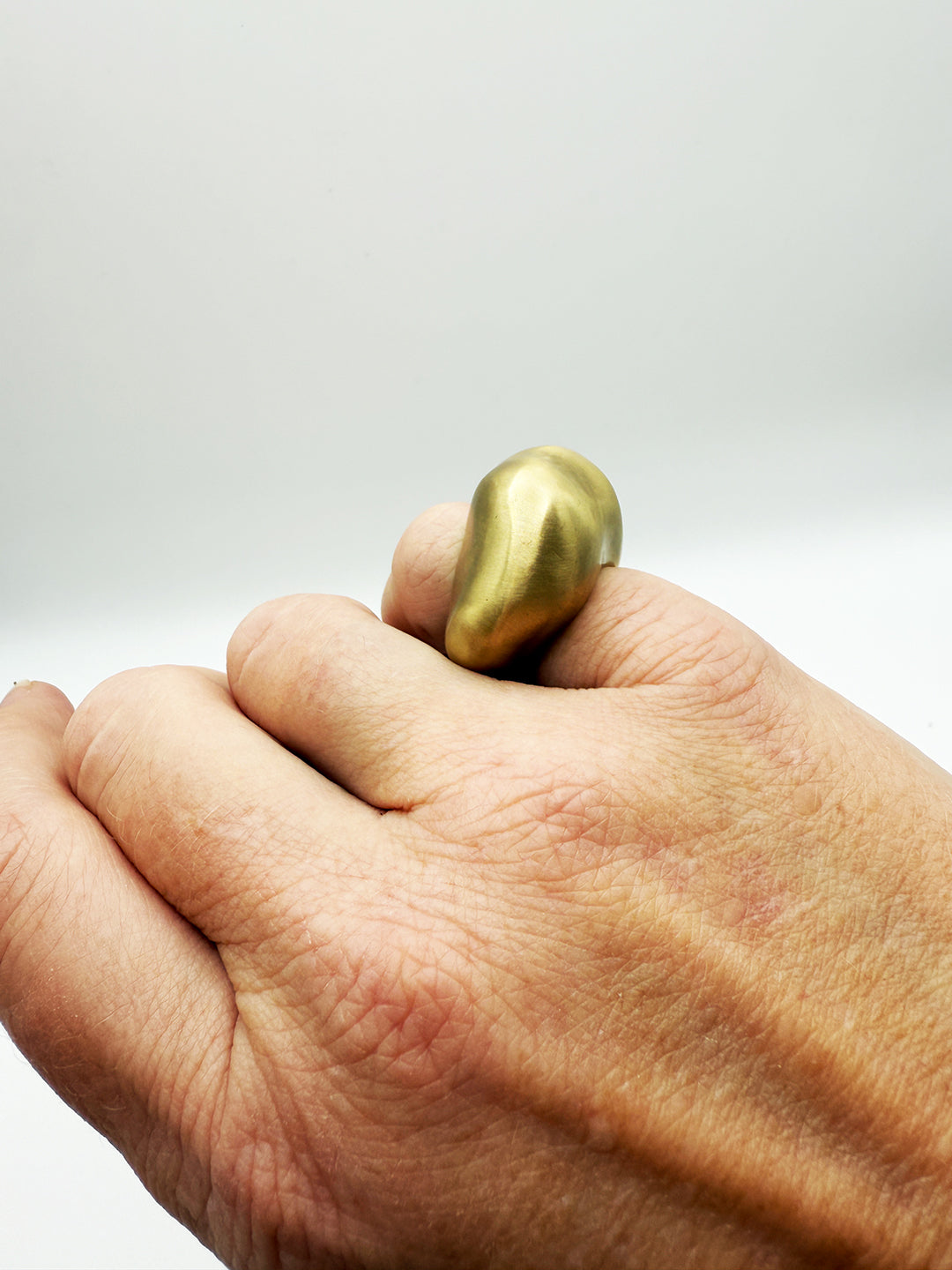 Hand holding a gold ring against a plain background