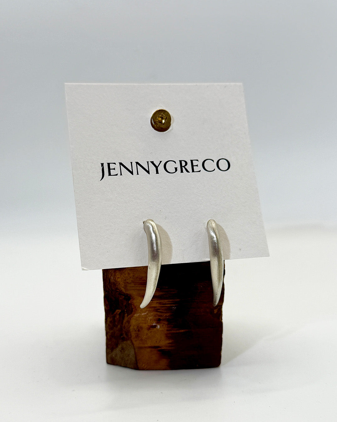 Jenny Greco earrings on a wooden stand with a white background
