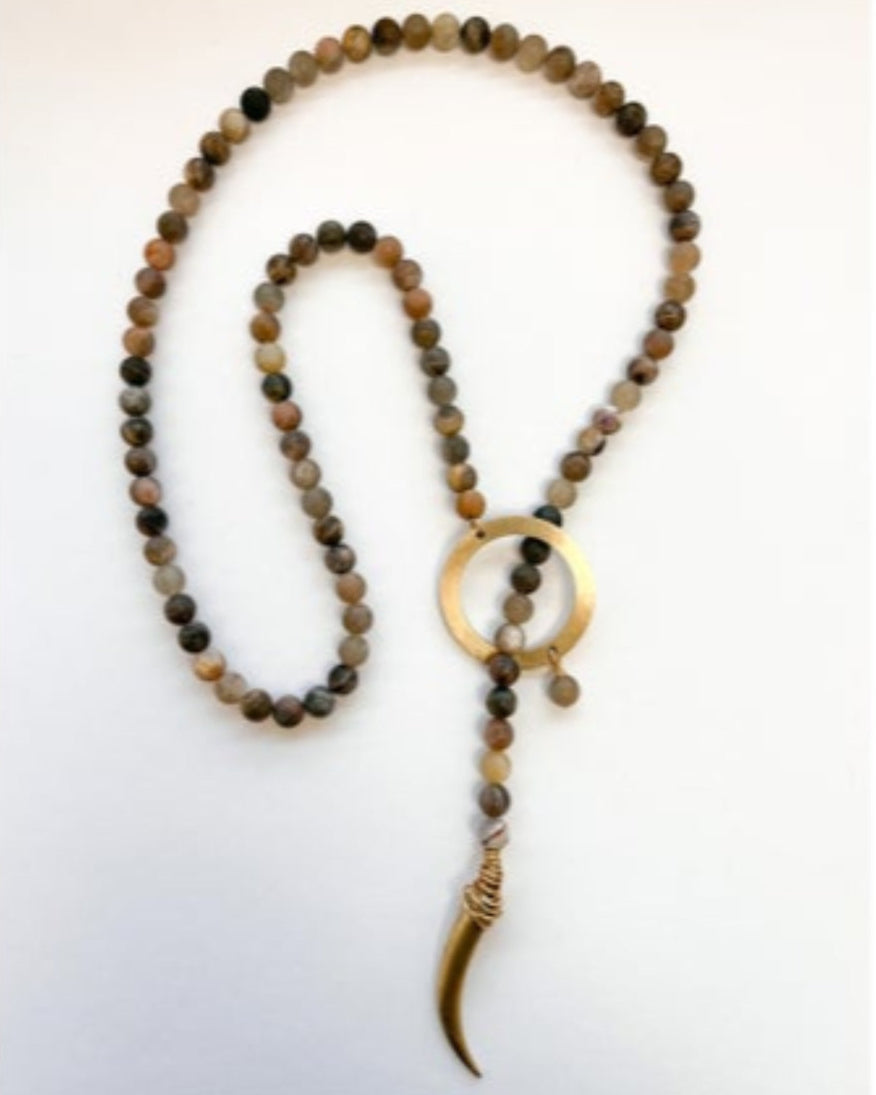 Beaded necklace with a circular gold accent and horn pendant on a white background