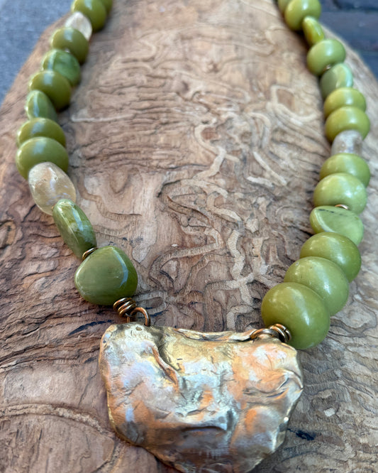 Necklace with green beads and a large bronze shell pendant on a wooden surface