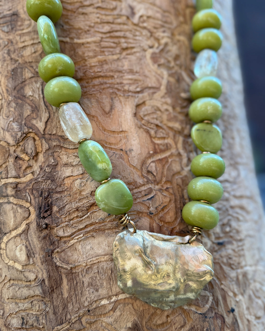 Necklace with green beads and a large bronze pendant on a wooden surface