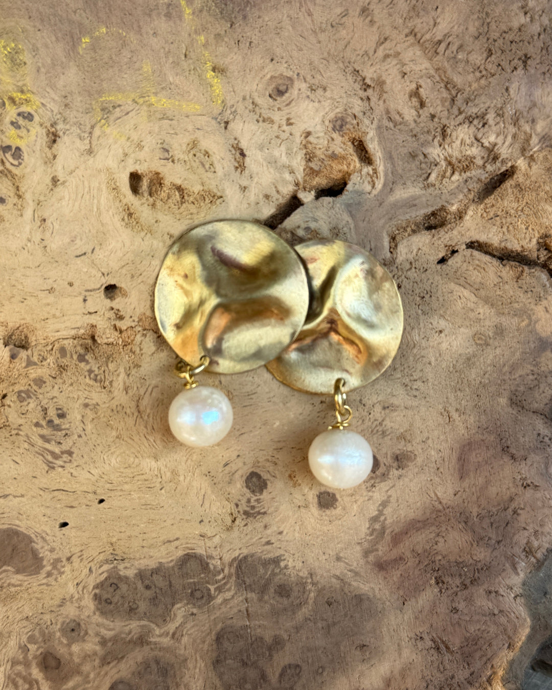 Gold earrings with pearl drops on a textured stone surface