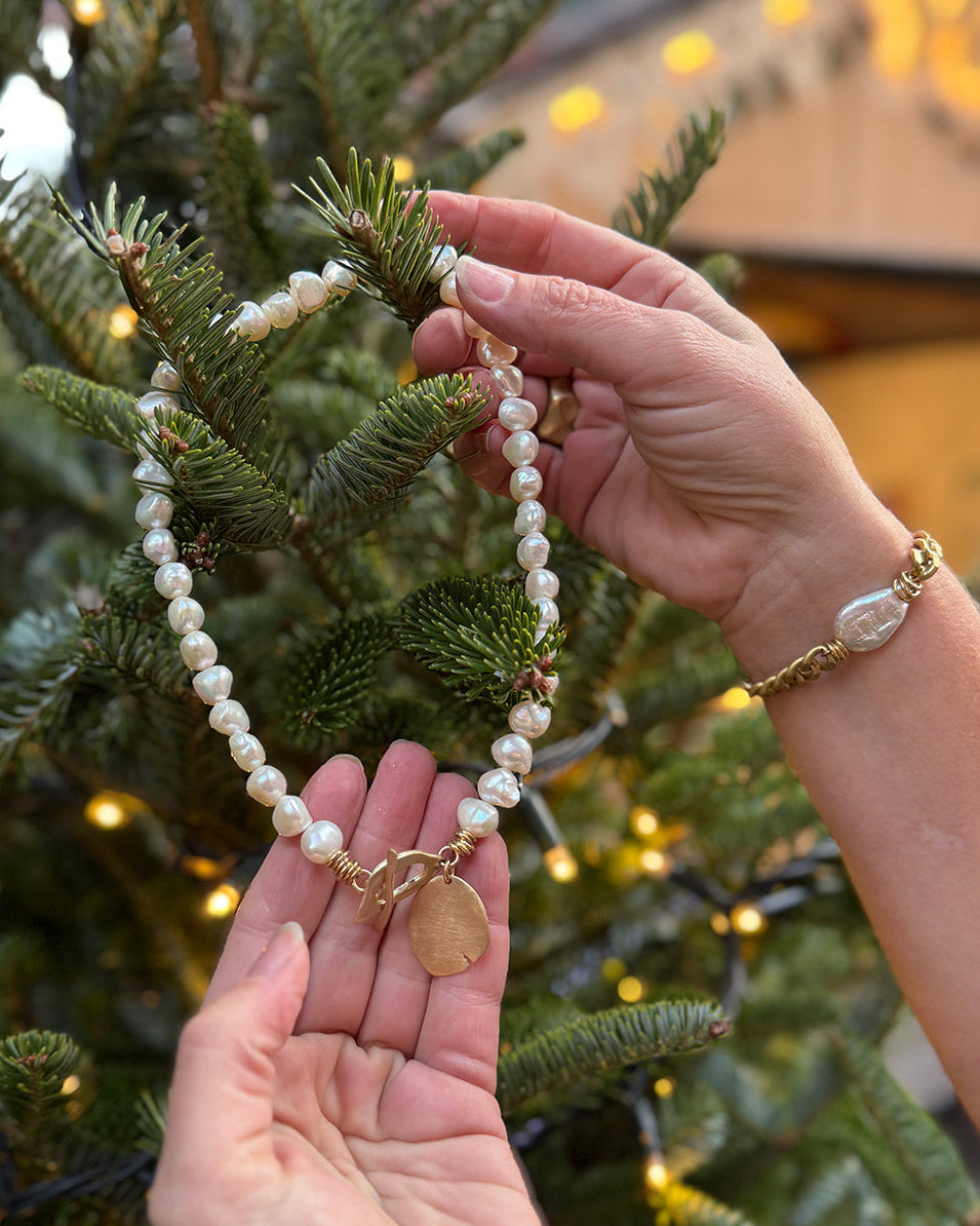 Person holding a pearl necklace with a gold charm against a Christmas tree background