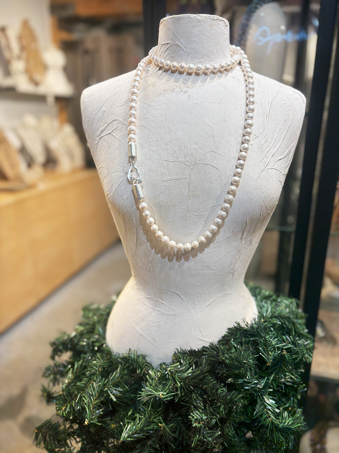 Pearl necklace on a mannequin bust with a green wreath skirt in a store setting