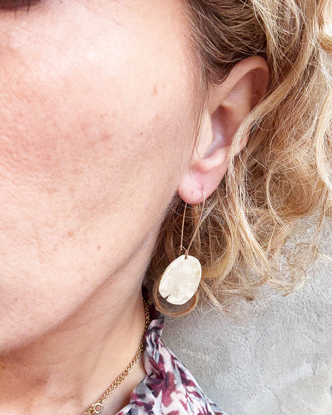 Close-up of a person wearing a gold earring with a beige stone on a neutral background