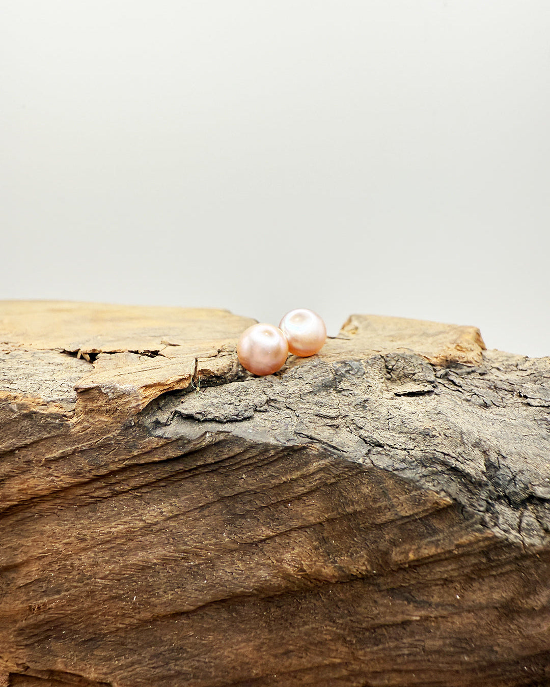 Two pink pearls on a piece of wood with a light gray background