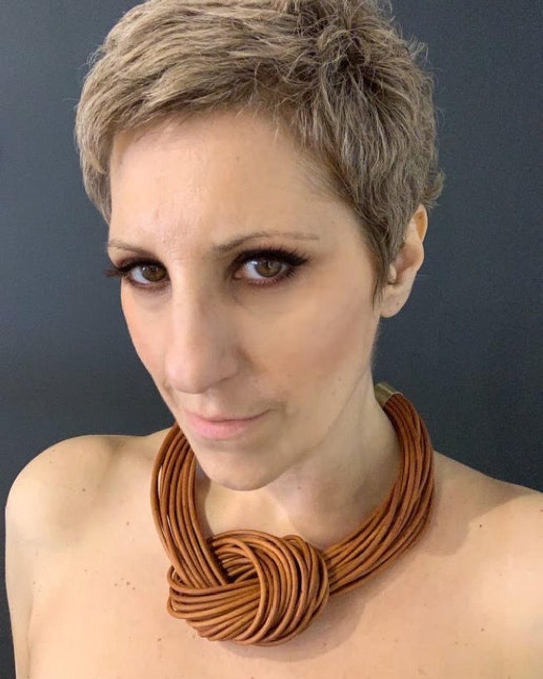Woman wearing a large brown  multistrand leather knotted necklace against a dark background