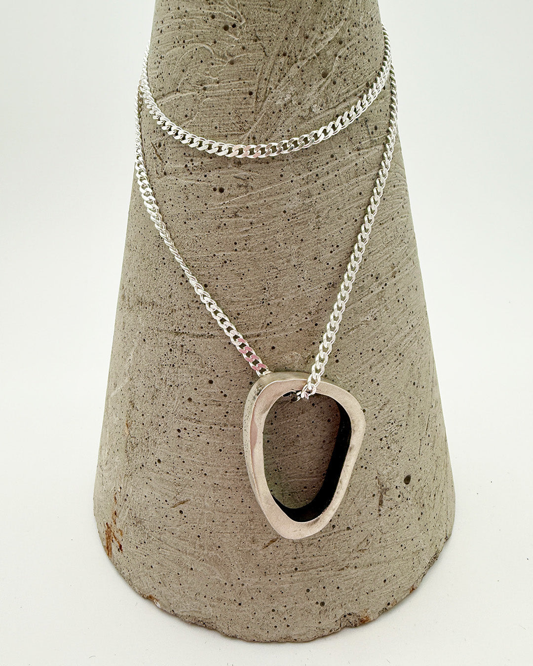 Silver necklace with a unique pendant on a textured stone stand against a white background