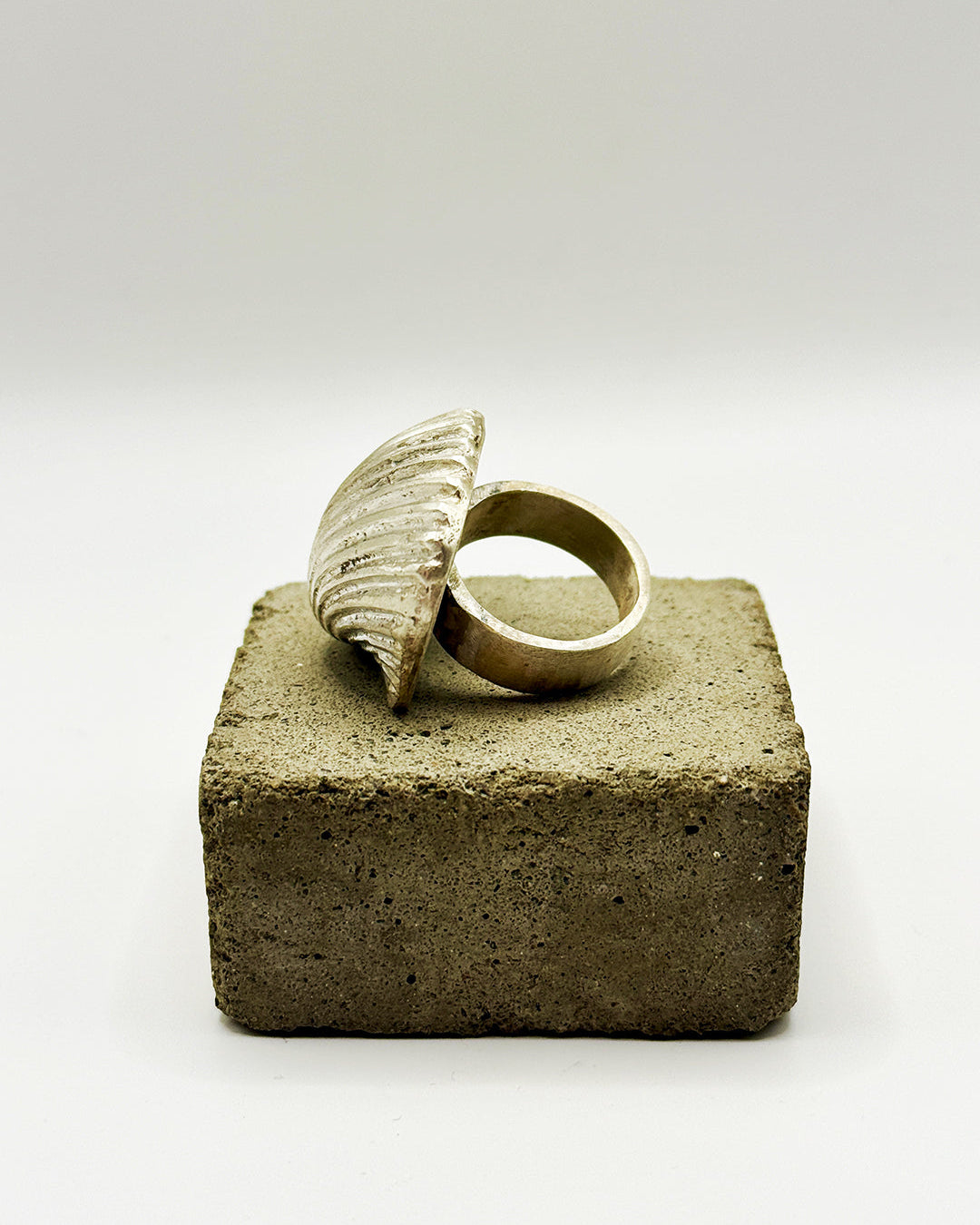 Gold ring with a shell-like design on a textured square block against a white background