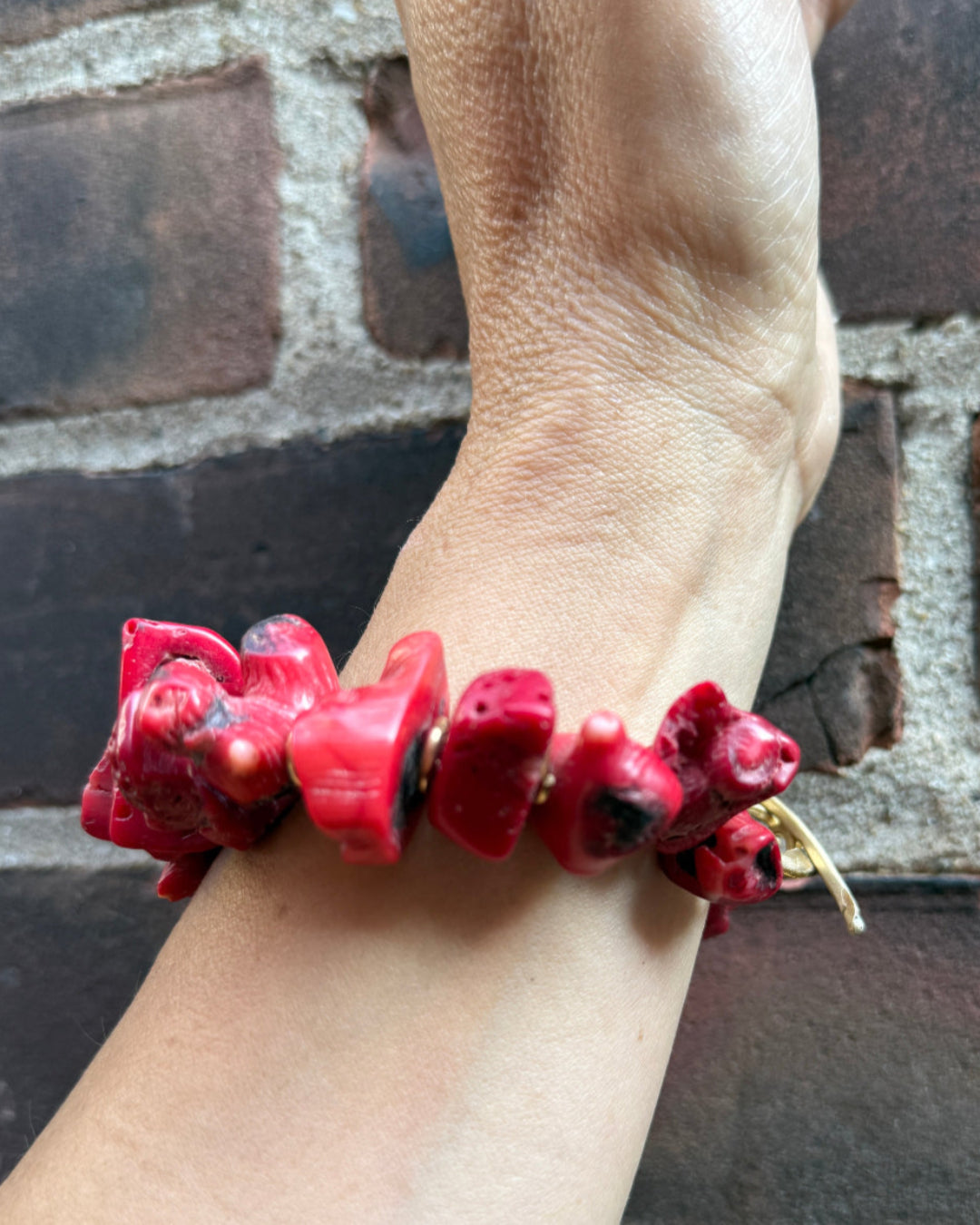 Red beaded bracelet on a wrist with a brick wall background