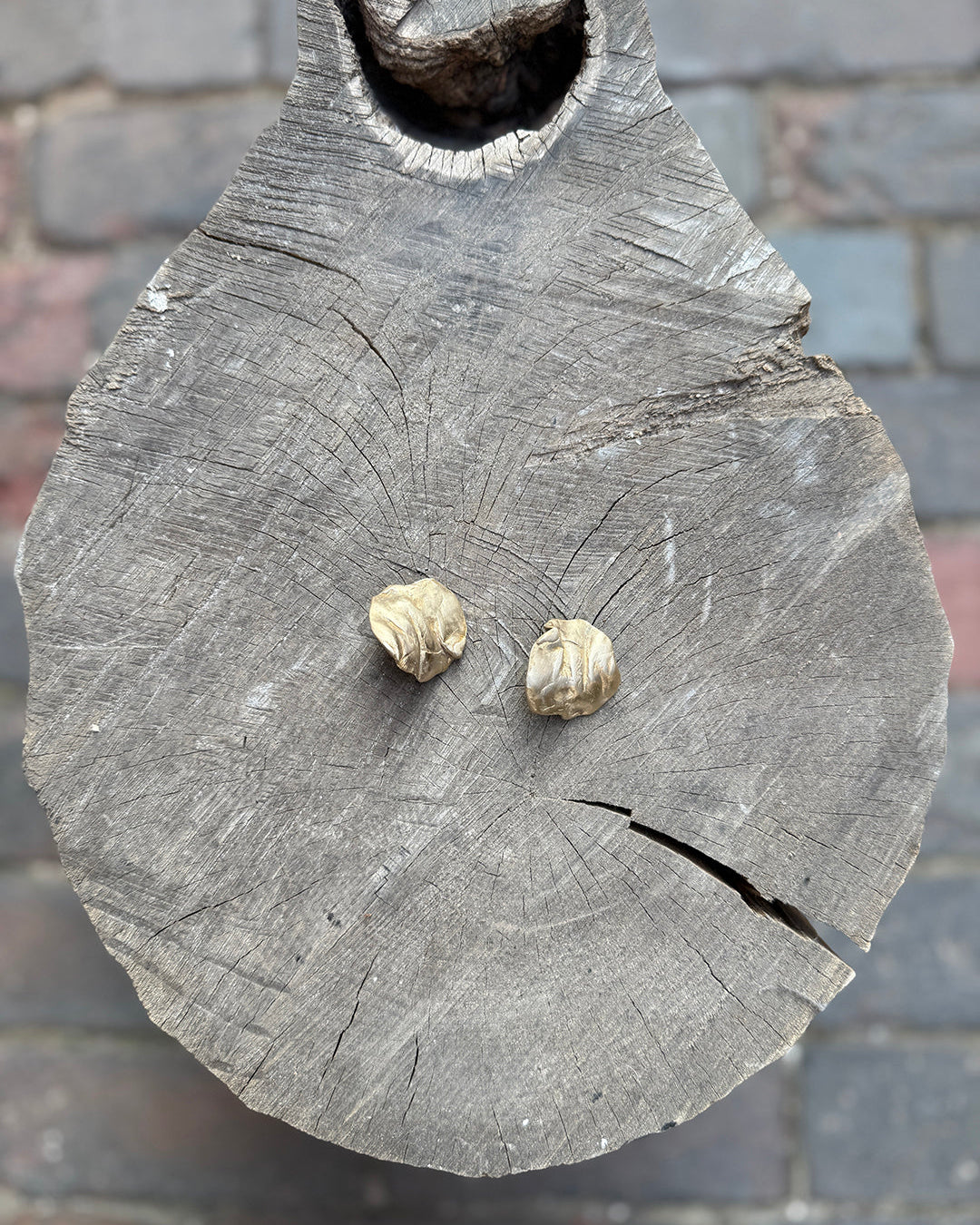 Two coral-inspired gold earrings on a wooden surface with a blurred background