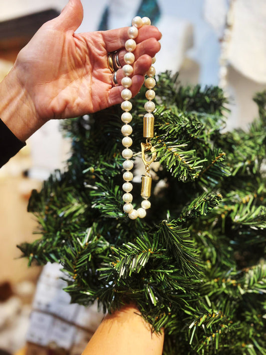 Hand holding a pearl necklace with a gold clasp against a blurred Christmas tree background