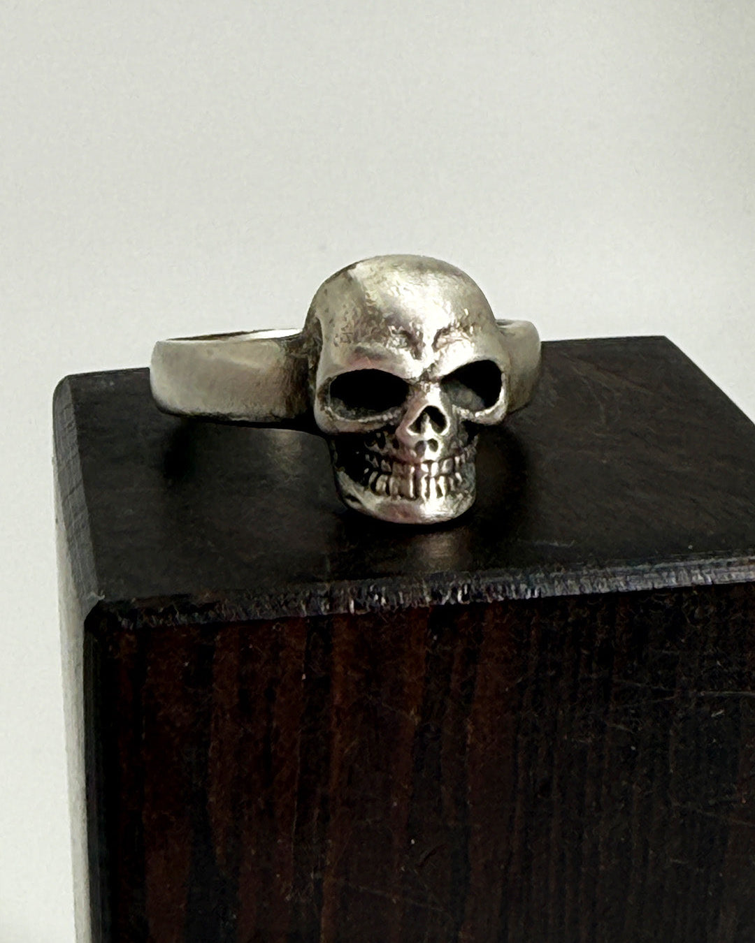 Silver skull ring on a wooden stand with a white background