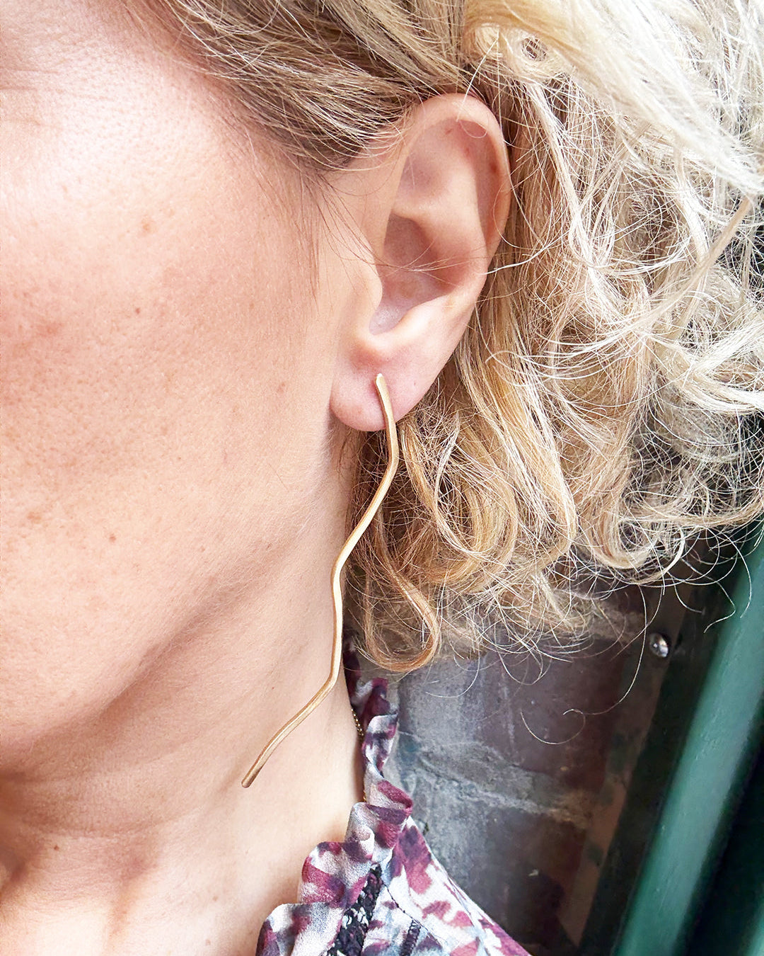 Close-up of a person's ear with blonde hair and a floral earring.