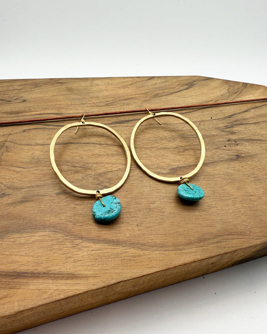 Gold hoop earrings with turquoise stones on a wooden surface