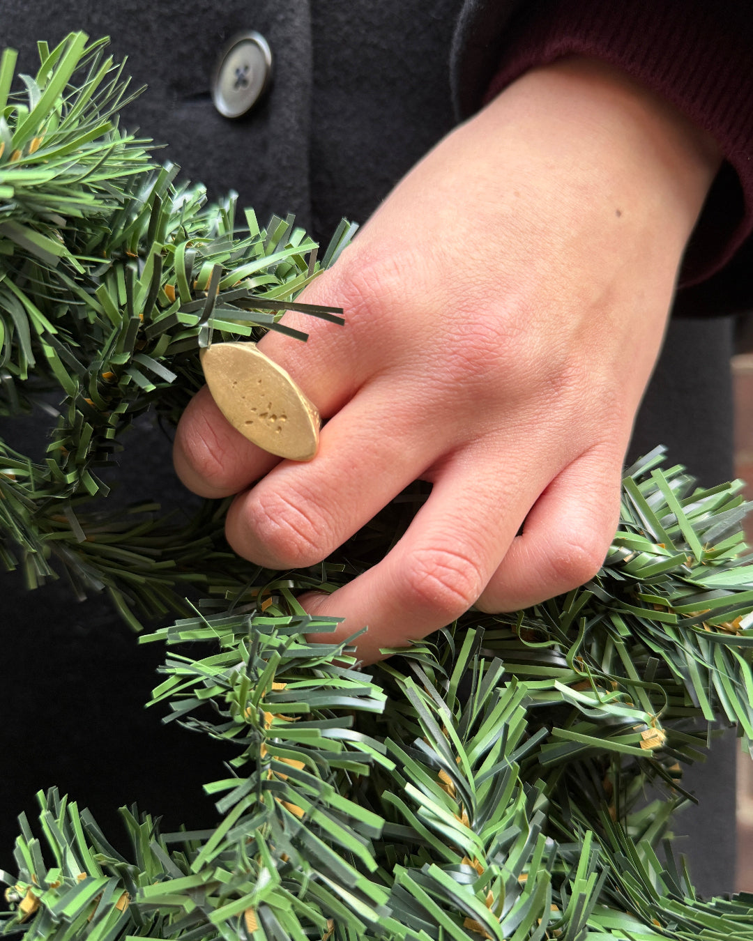 Hand adjusting a small gold ornament on a green wreath.