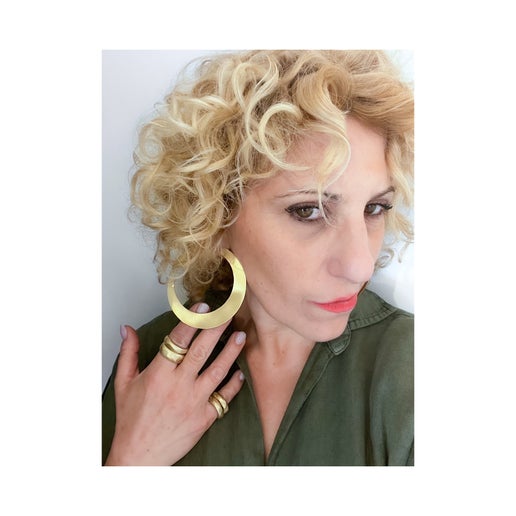 Woman wearing large bronze hoop earrings and multiple gold rings on a white background