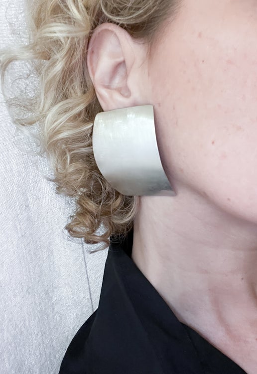 Close-up of a person wearing a large curved rectangular silver earring against a neutral background