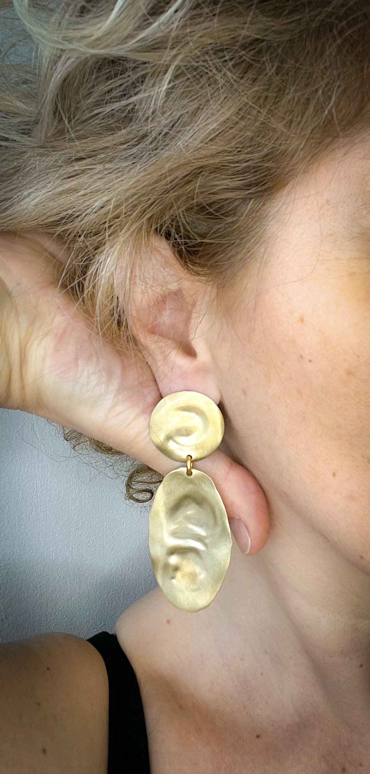 Close-up of a person wearing  textured gold earrings with a neutral background