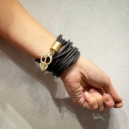 Hand wearing a black multi-strand leather bracelet with gold clasp on a neutral background