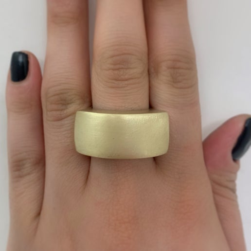Gold statement ring on a person's finger against a white background