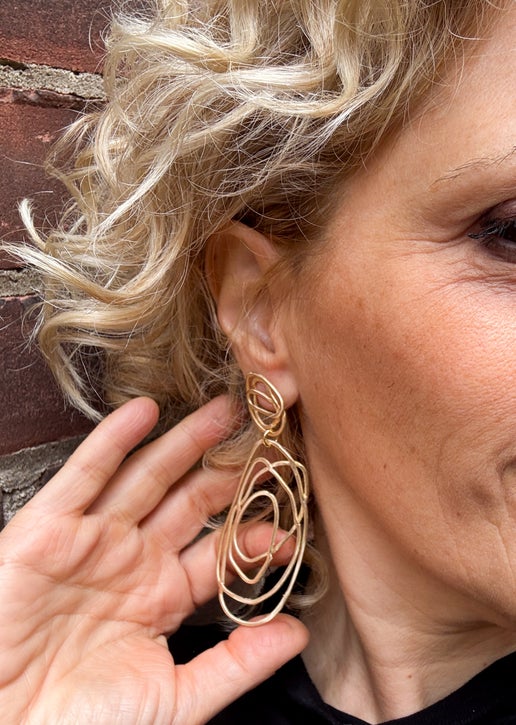Close-up of a woman wearing gold wire hoop earrings against a brick wall