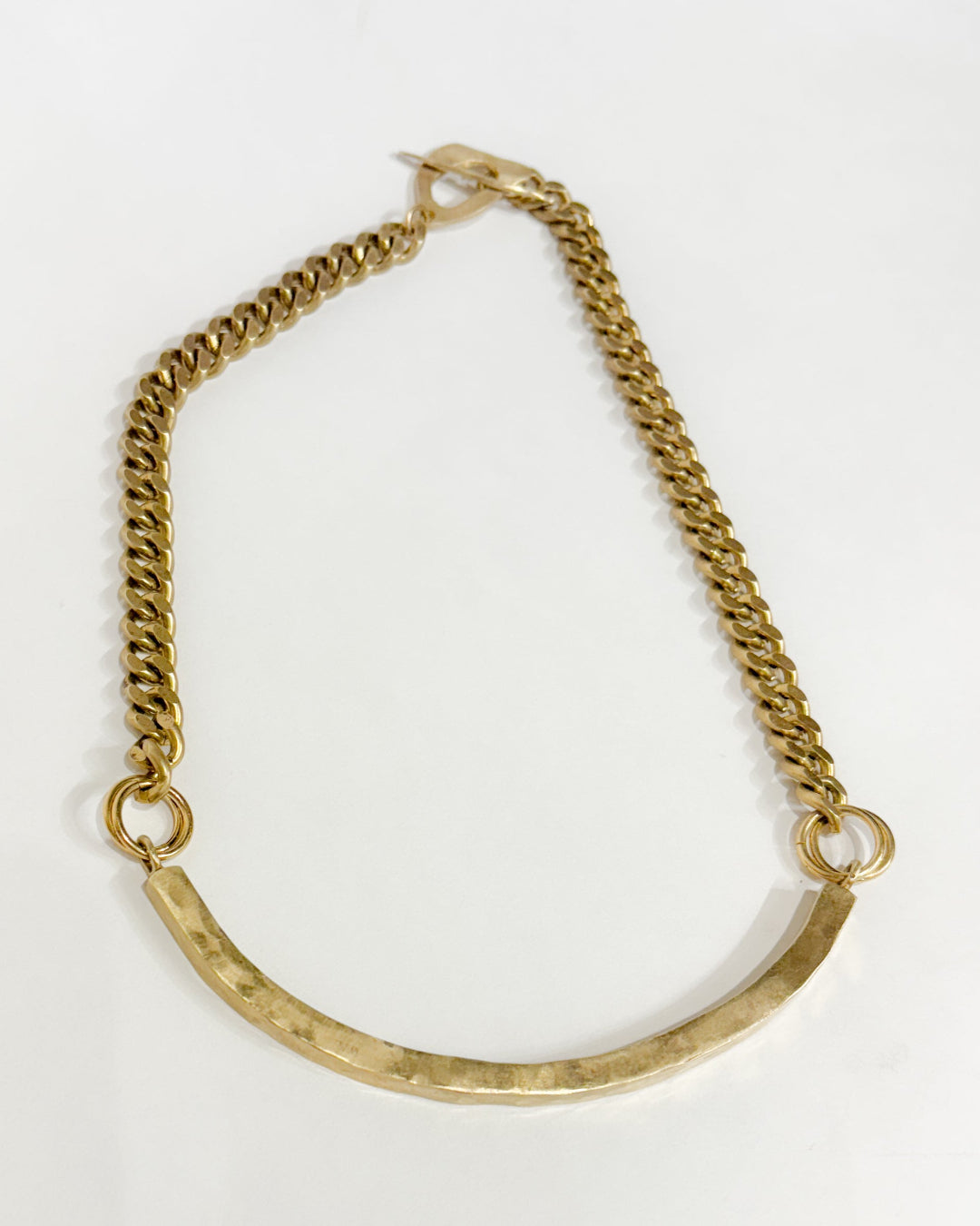 Gold necklace wiith a curved design on a white background