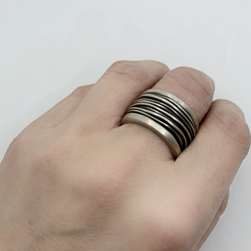 Hand wearing a bronze ring with wire detailing on a white background