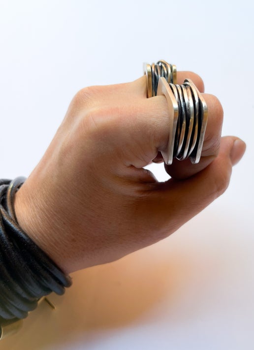 Hand wearing multiple statment rings on a plain background