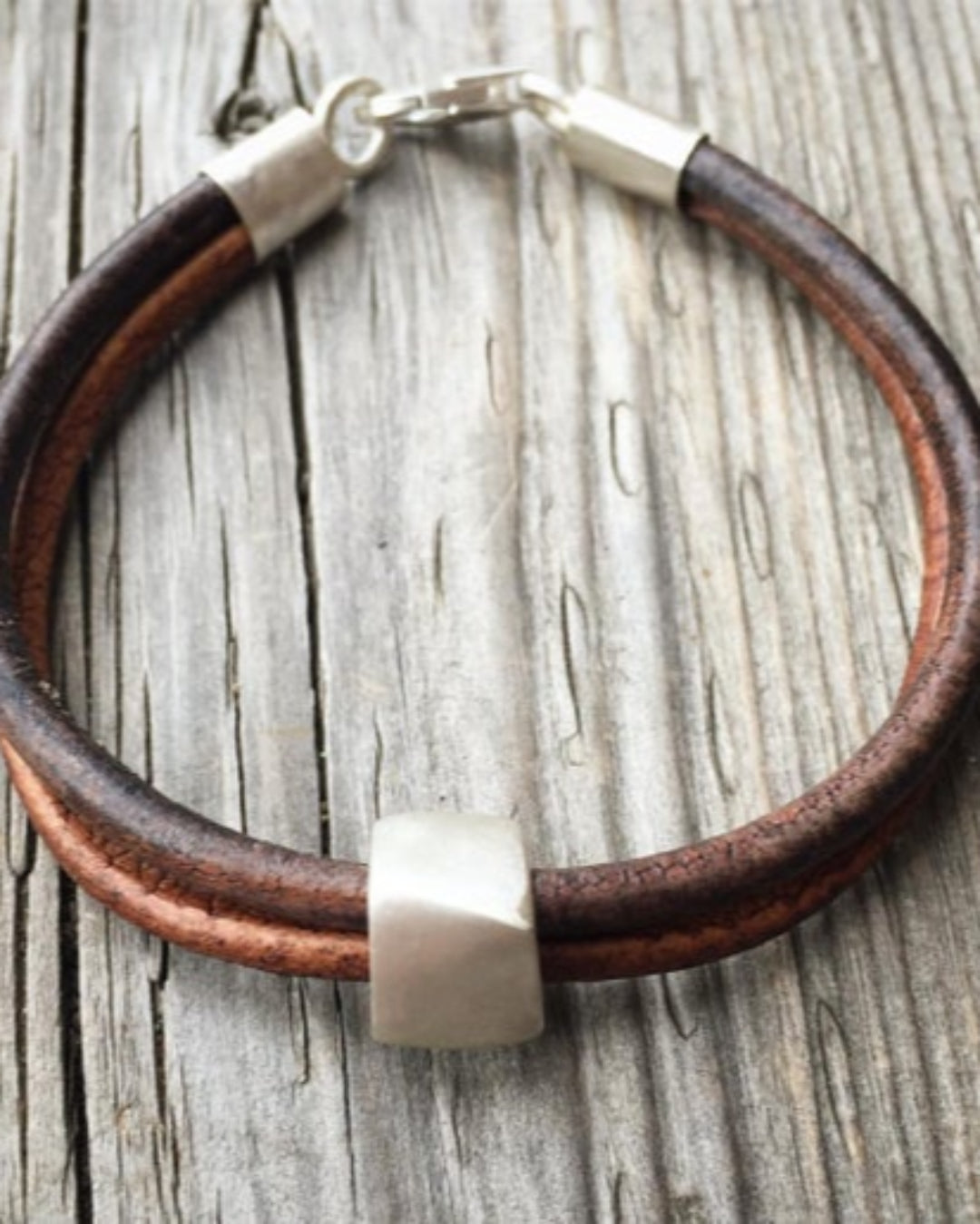 Brown leather bracelet with silver clasp on a wooden surface