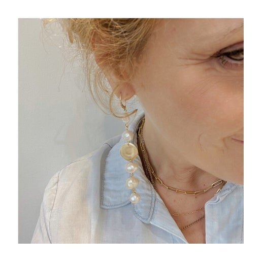 Close-up of a person wearing pearl and gold drop earrings against a light background