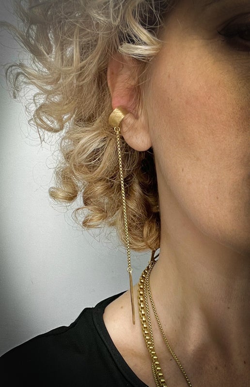 Close-up of a person wearing a gold ear cuff with a dangling chain.