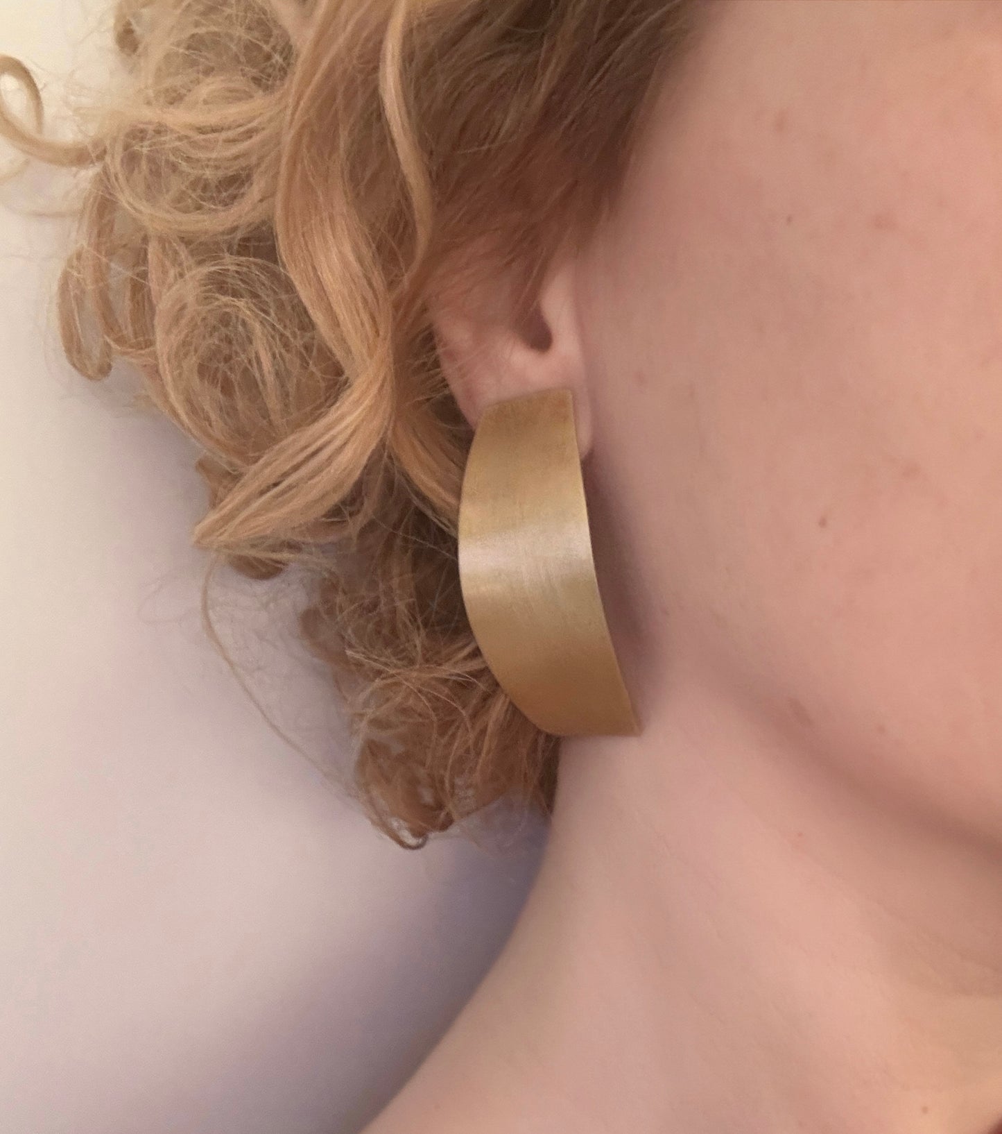 Curved bronze earring worn by a person with blonde hair.