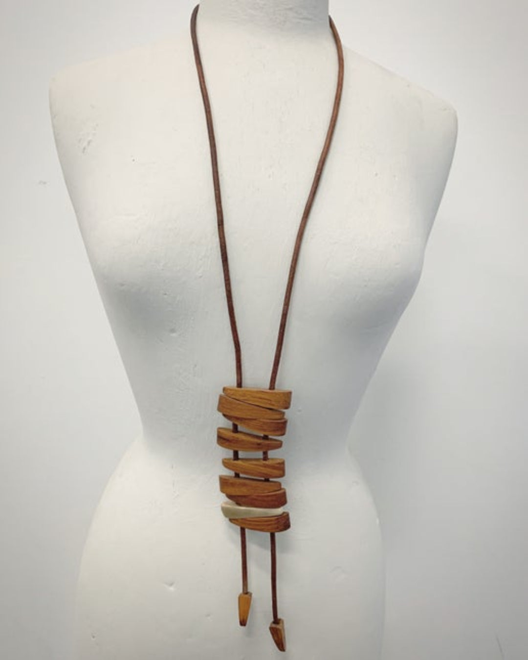 Brown leather cord necklace with wooden and bronze details on a mannequin against a white background
