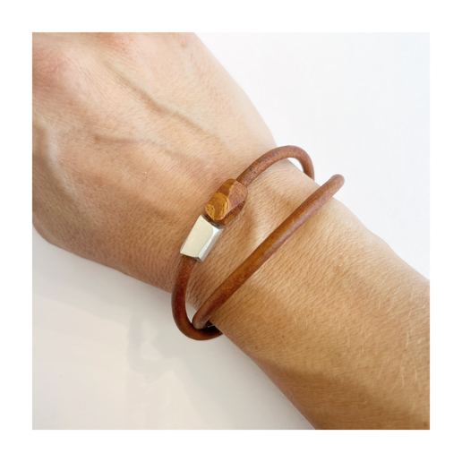 Brown double wrap leather bracelet with a silver clasp on a wrist against a white background