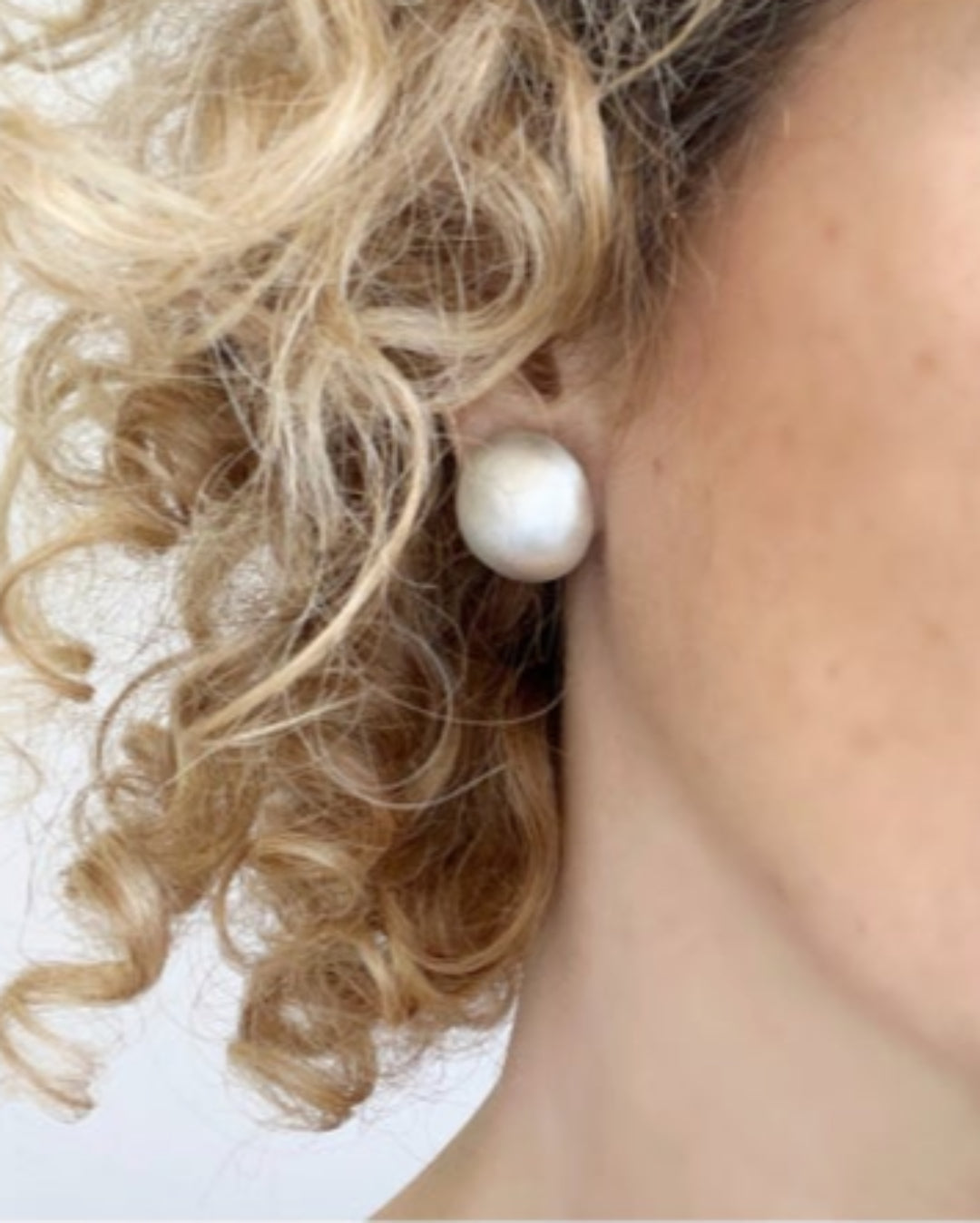 Close-up of a person wearing an oversized sterling silver stud earring with blonde hair.