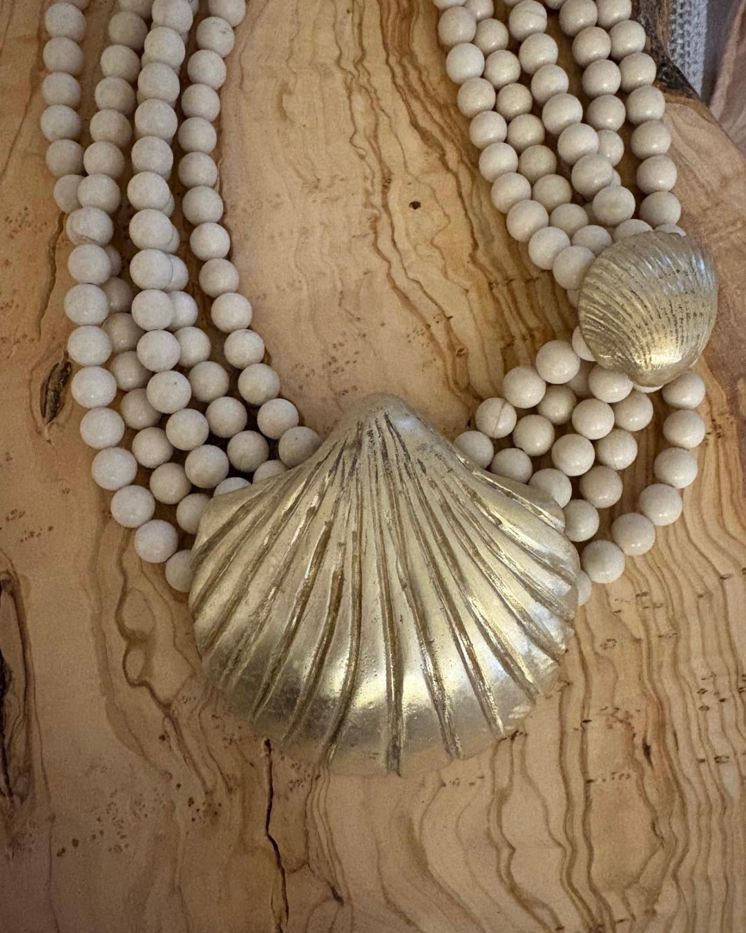 Necklace with white beads and gold shell pendants on a wooden surface