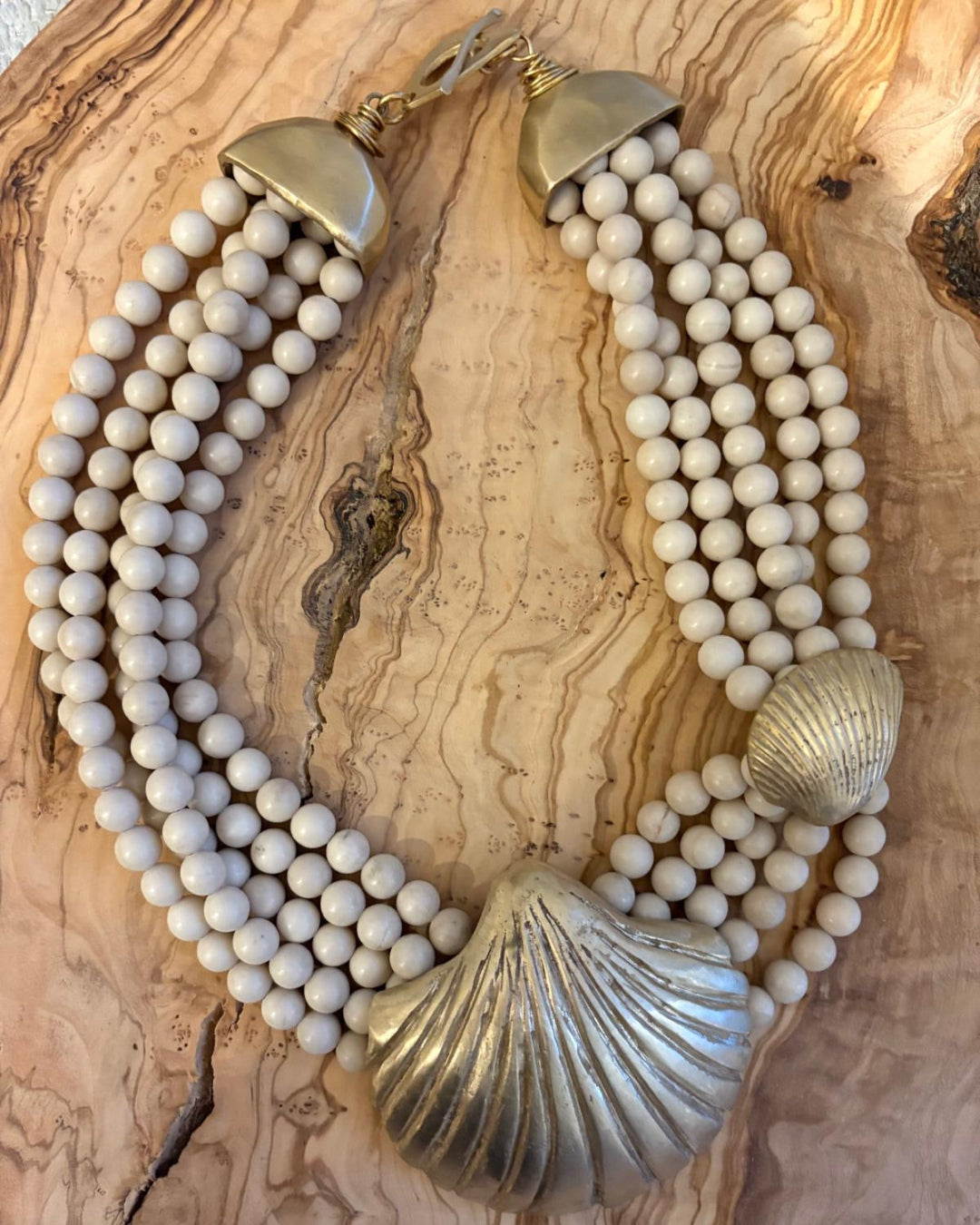 Necklace with white beads and gold shell details on a wooden surface