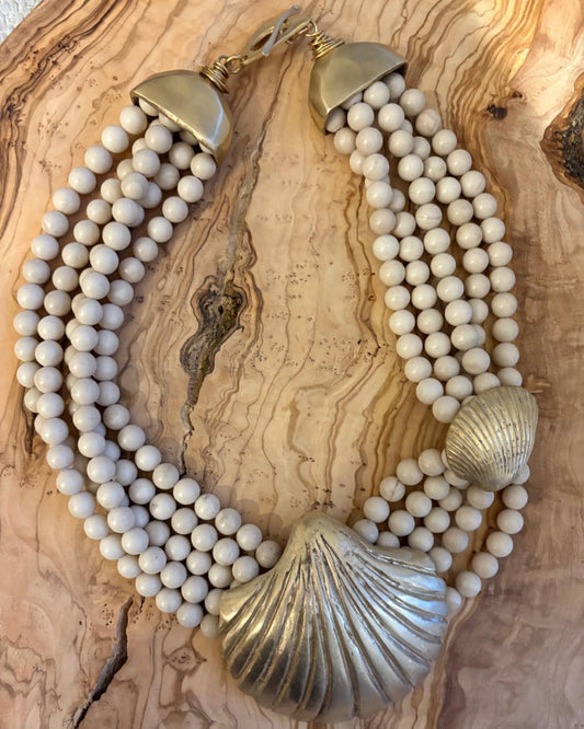 Necklace with white beads and gold shell details on a wooden surface
