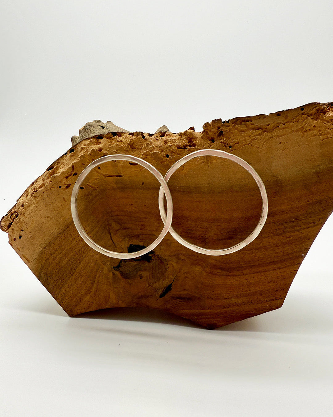 Two gold hoop earrings on a wooden block with a white background