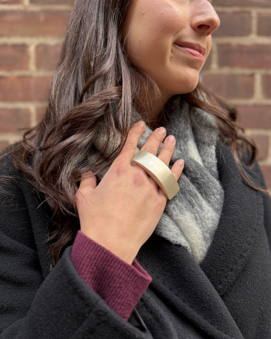 Woman wearing a dark coat and gray scarf with a brick wall background
