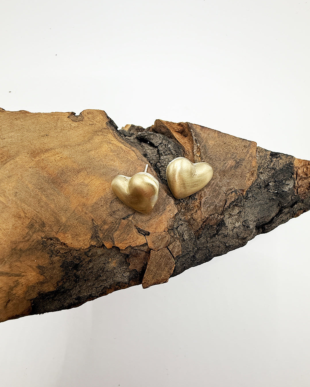 Gold heart-shaped earrings on a piece of wood with a white background
