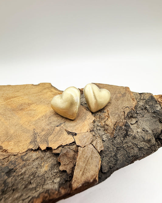 Gold heart-shaped earrings on a wooden surface with a white background