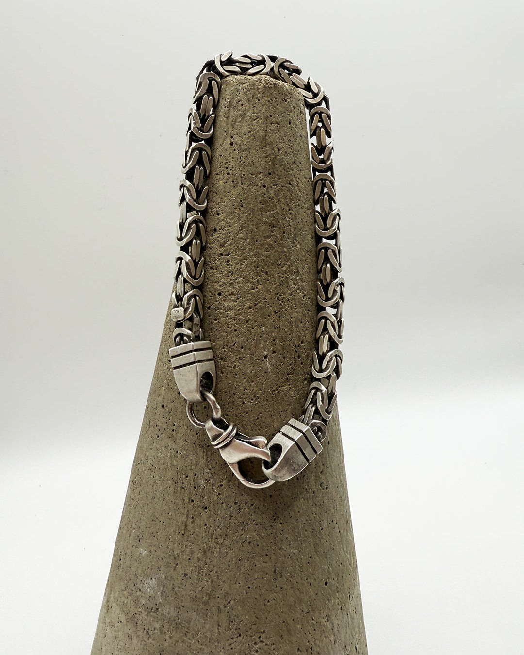 Silver chain necklace on a textured gray stand with a white background