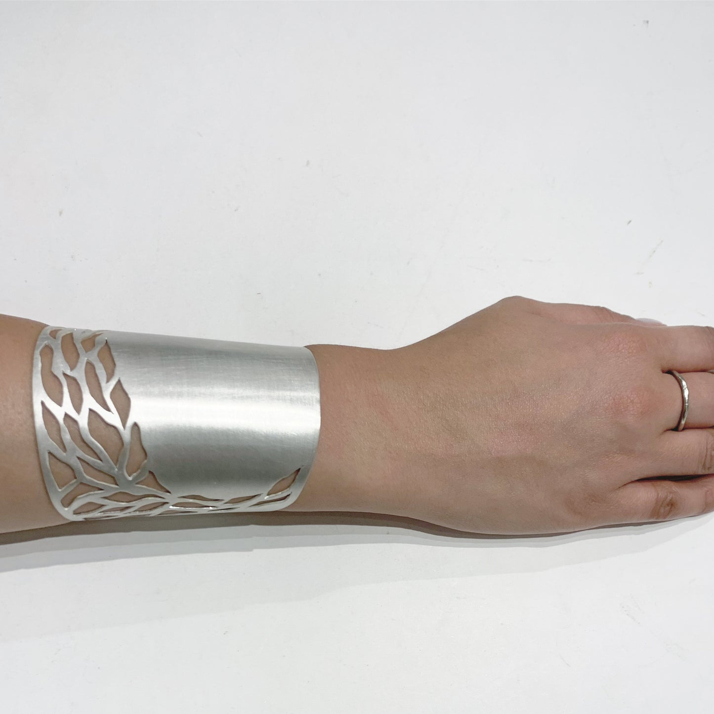 Silver cuff bracelet with leaf pattern on a wrist against a white background