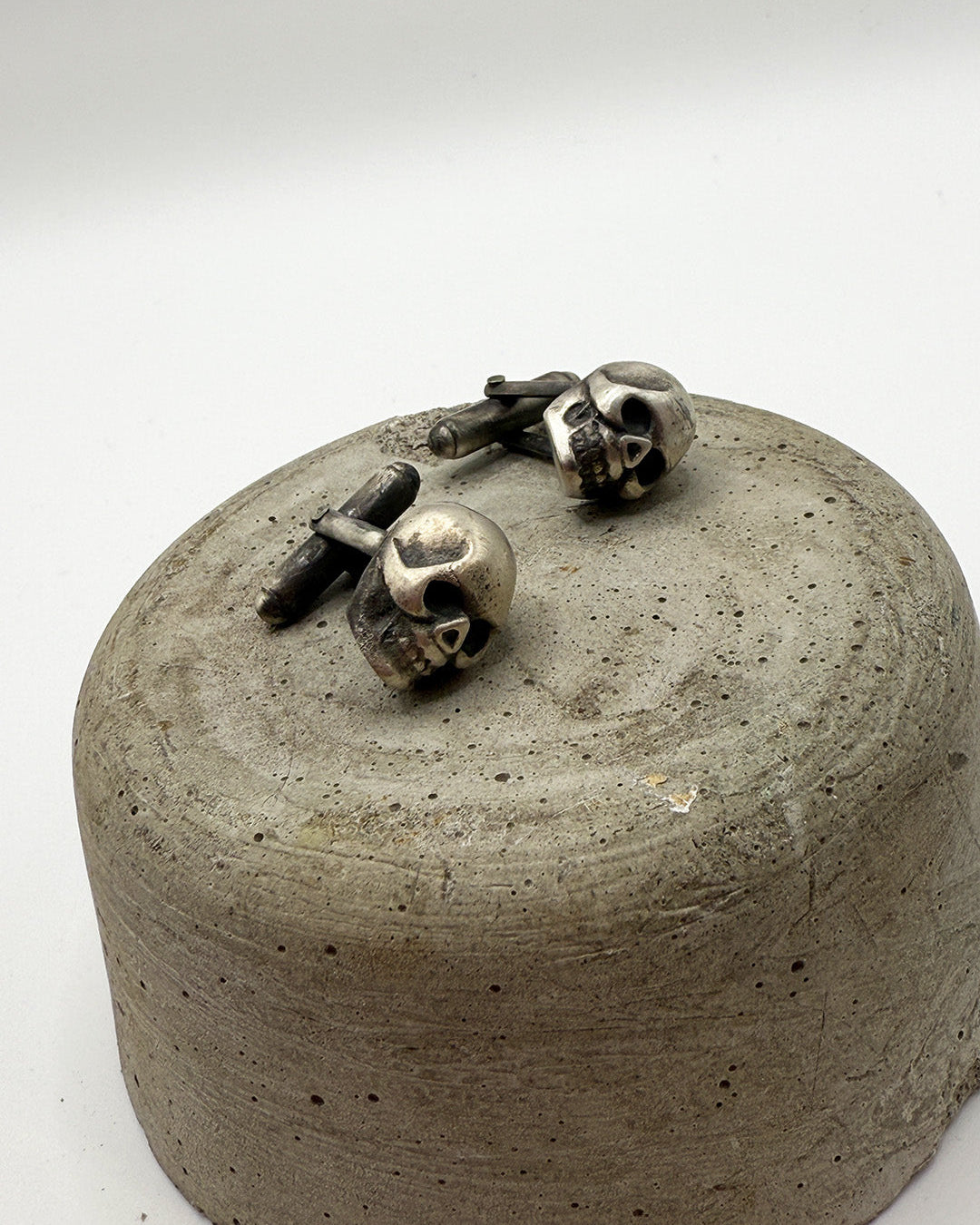 Silver skull-shaped cufflinks on a concrete block with a white background