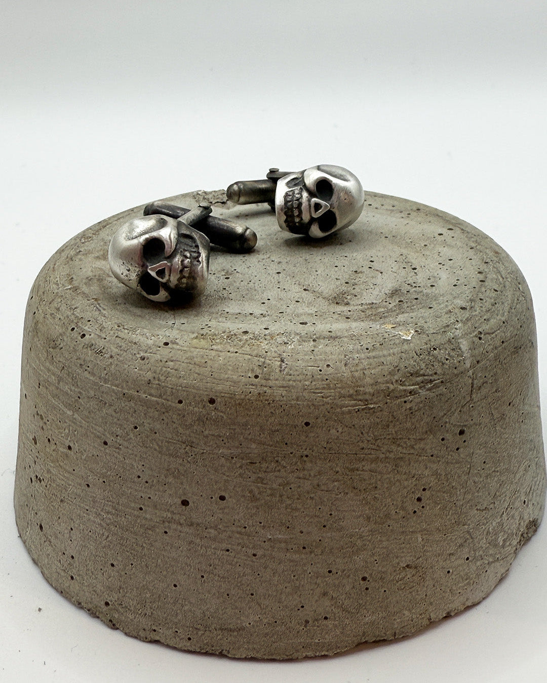 Skull-shaped cufflinks on a concrete block with a white background