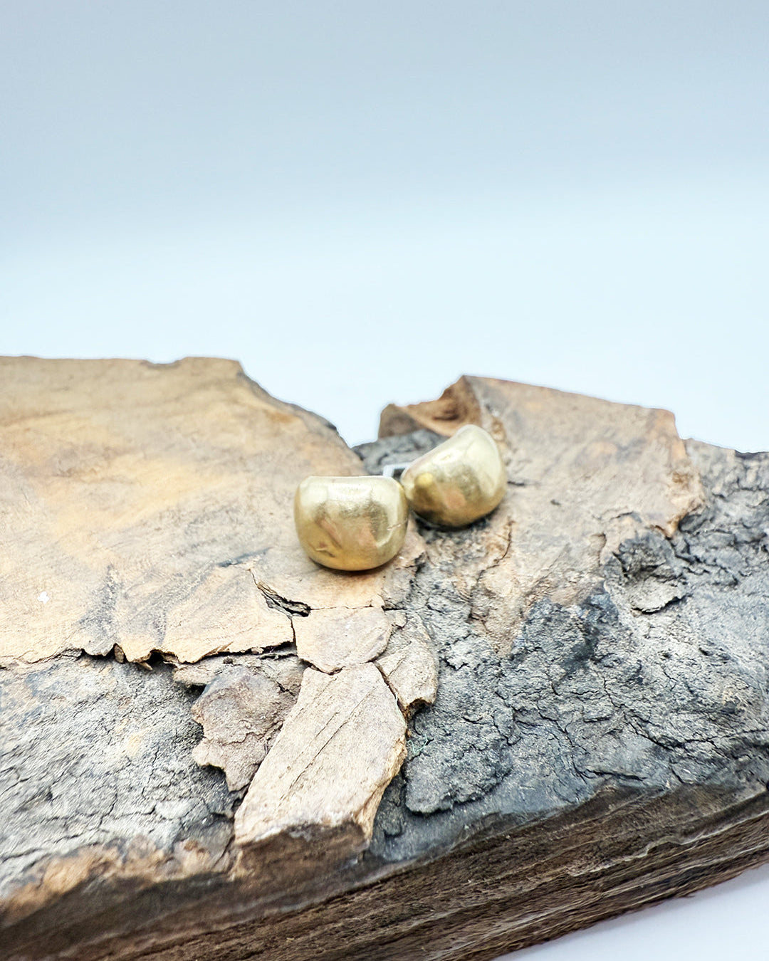 Gold earrings on a piece of textured wood with a light blue background