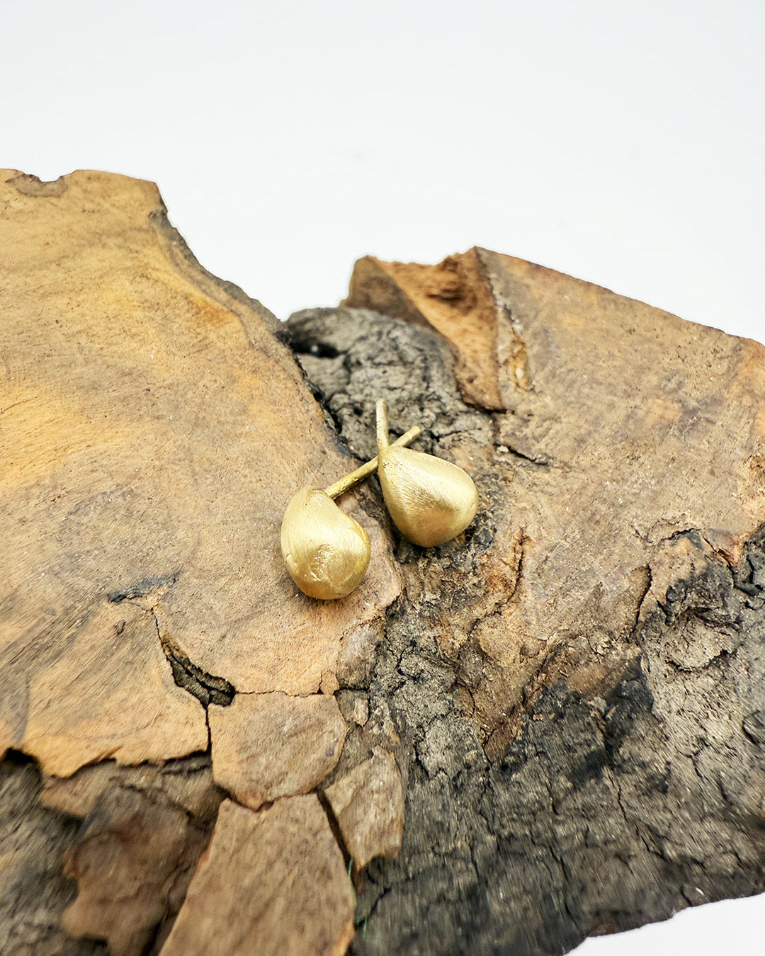 Gold earrings on a textured wooden surface
